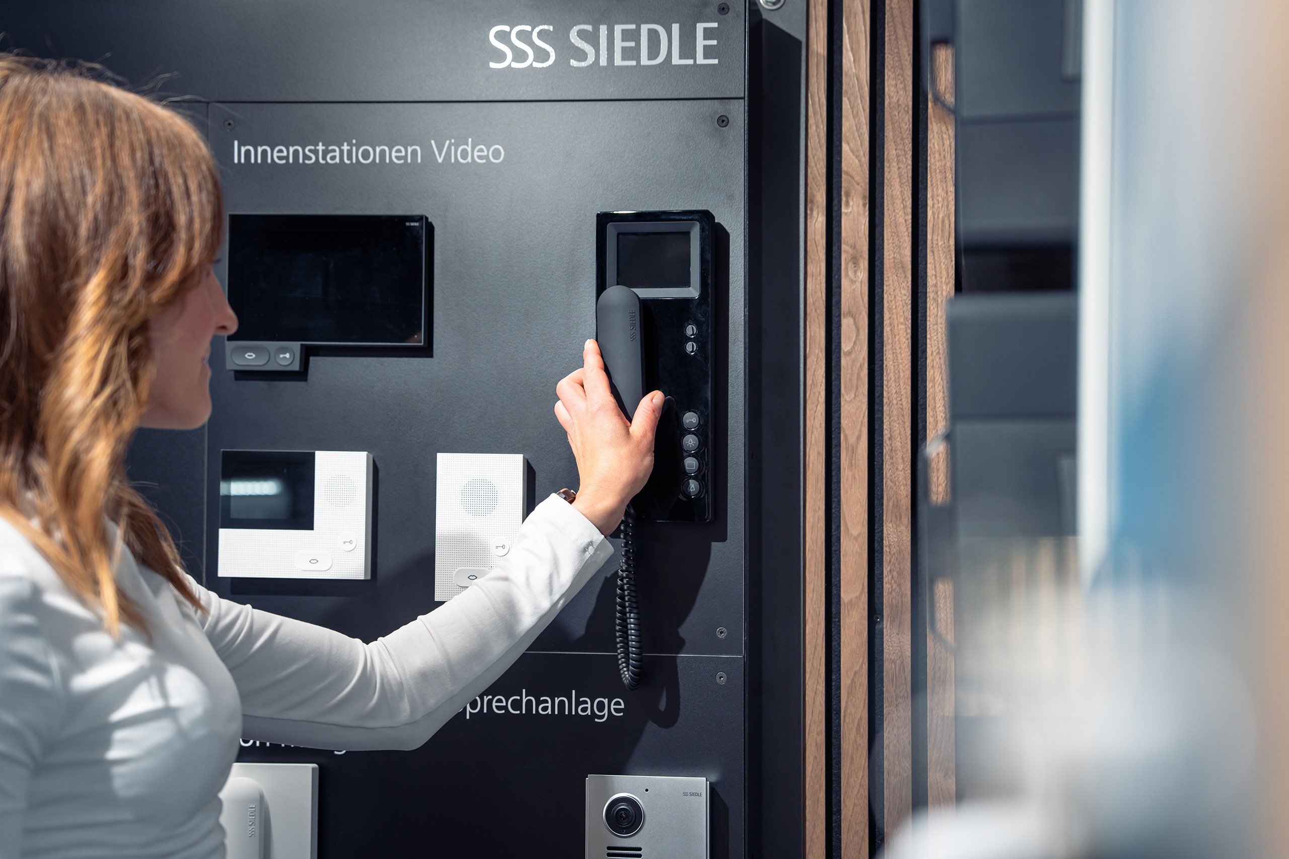 Frau bedient Siedle-Sprechanlage mit Videostation an Musterwand
