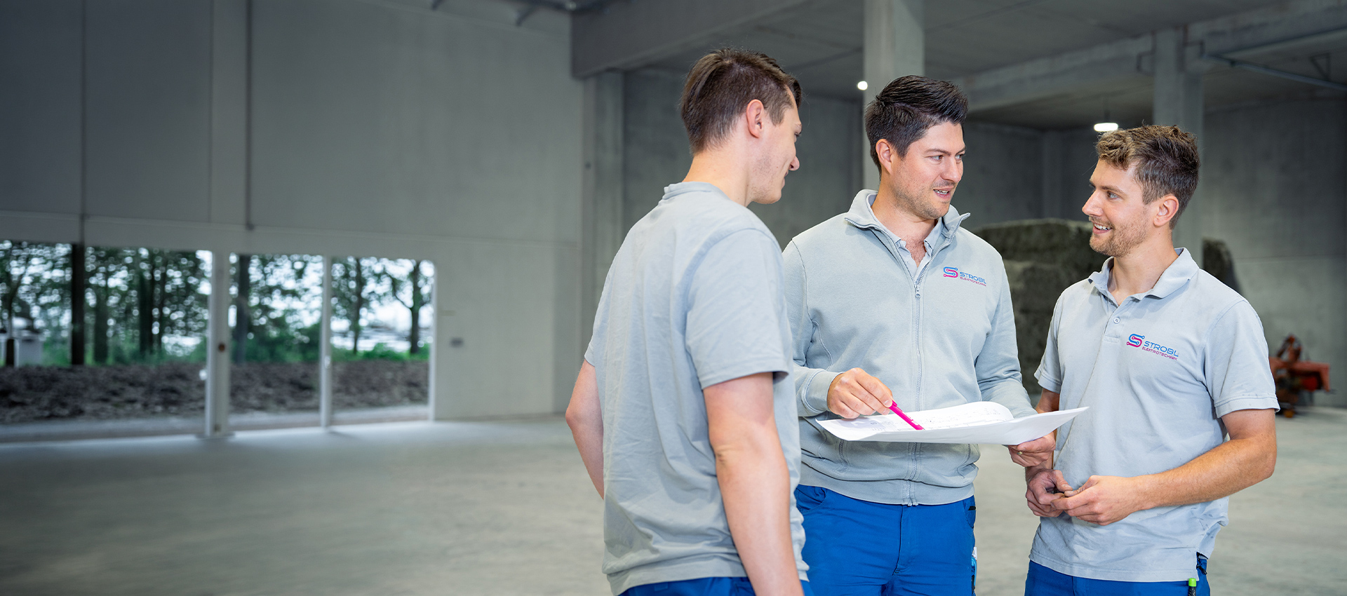 Drei Mitarbeiter besprechen Baupläne in einer leeren Halle