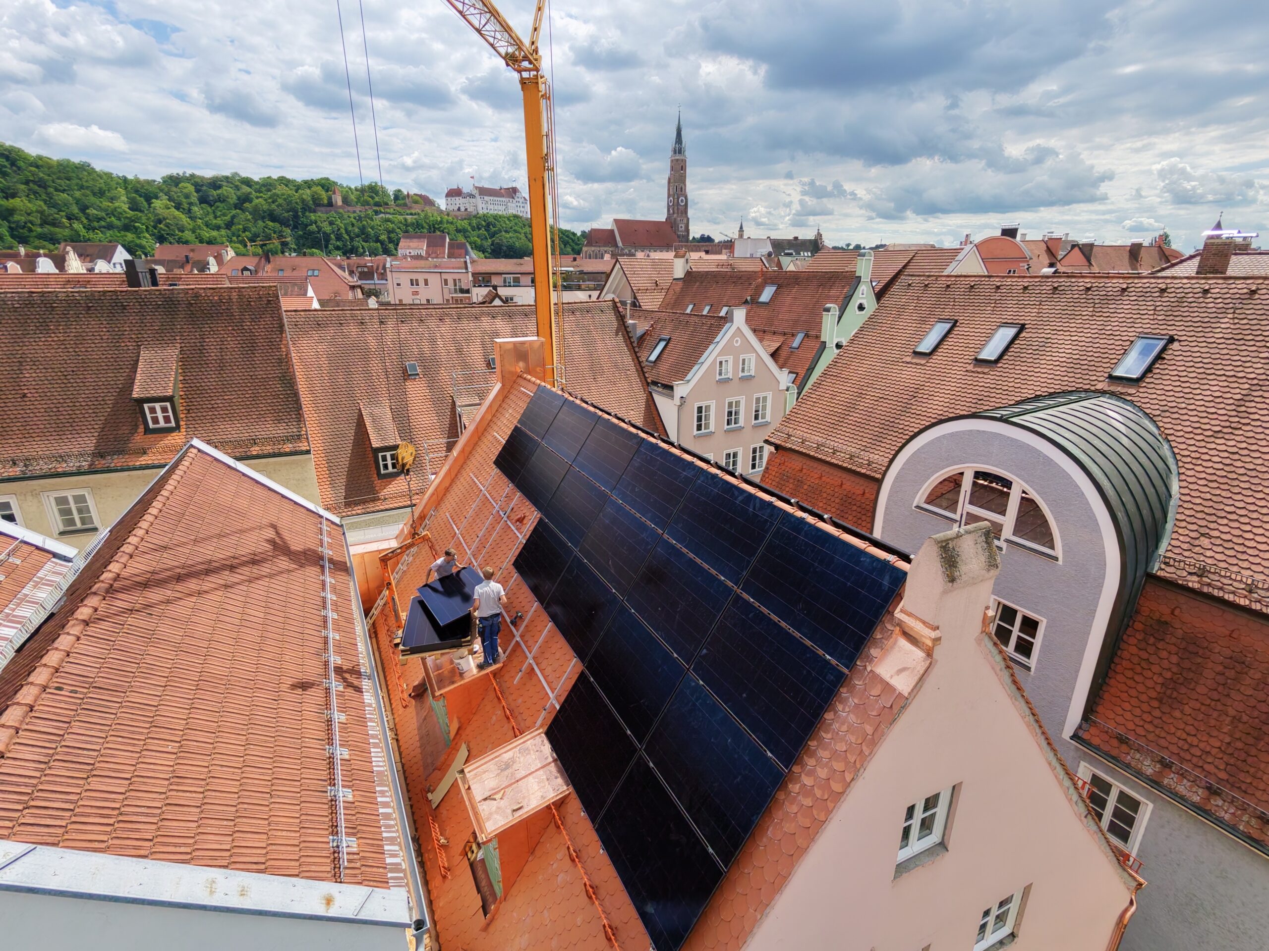 Monteure setzen Solarmodule auf Dach, Blick über Landshuter Dächer mit Burg Trausnitz