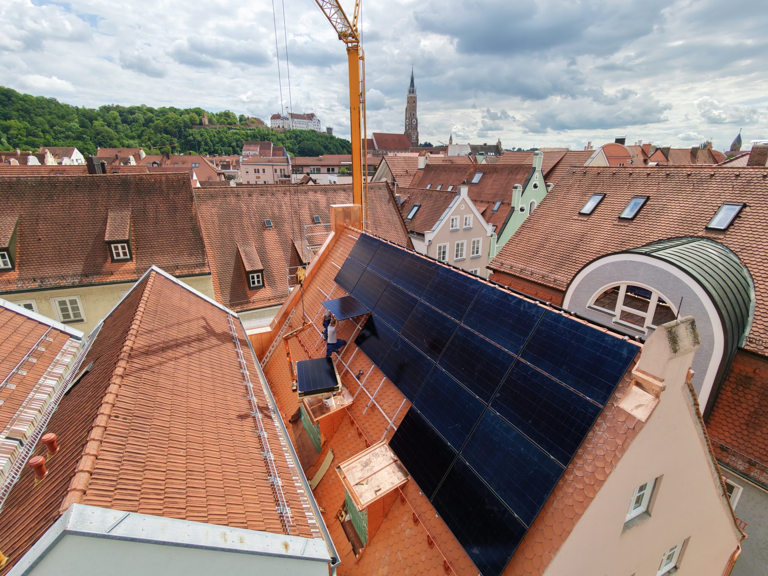 Photovoltaik-Montage auf Dach mit Kran, Panorama der Landshuter Altstadt mit Burg und Kirchturm