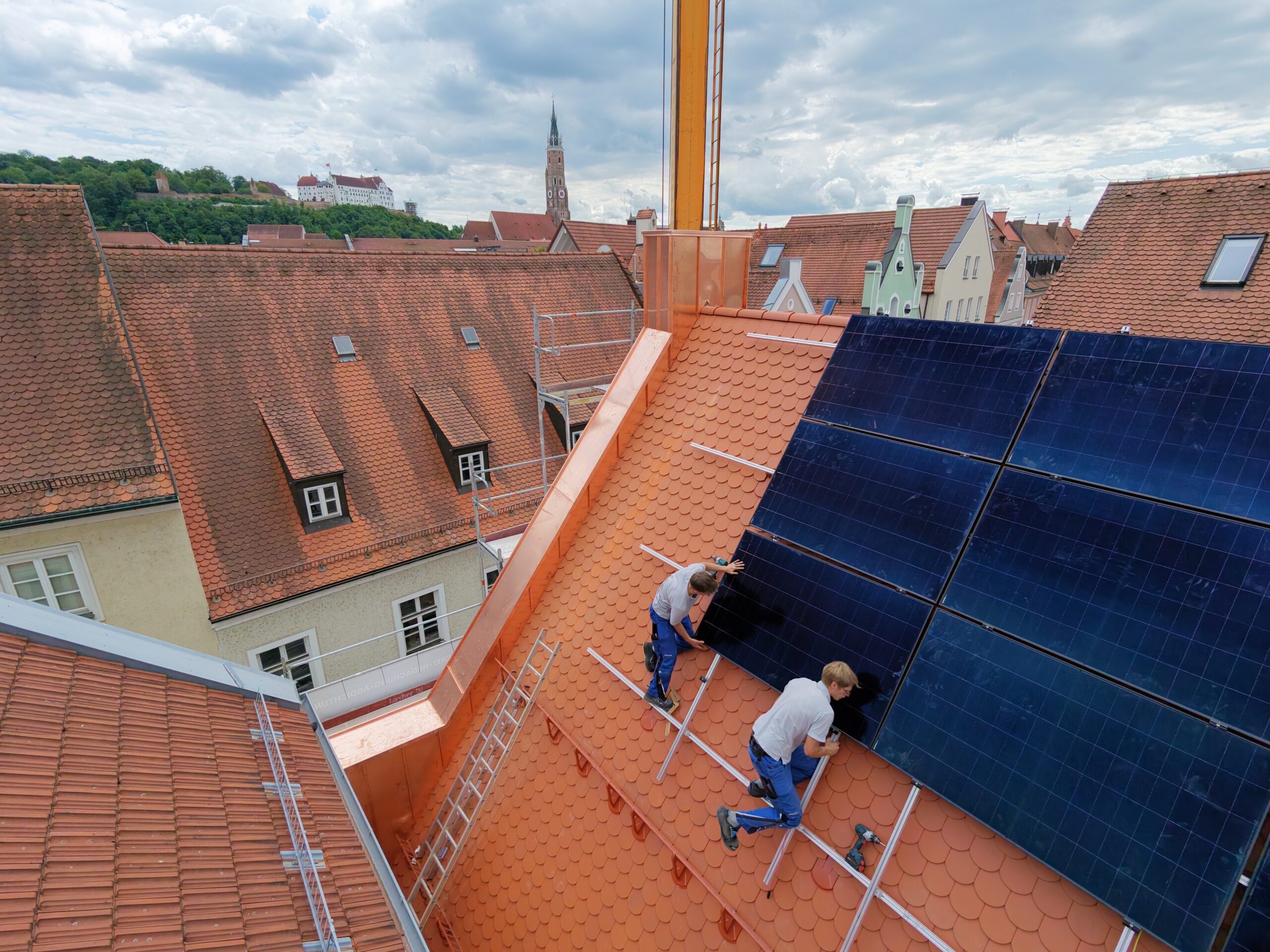 Monteure installieren Solarmodule, Blick über Landshut mit Burg Trausnitz und Martinskirche