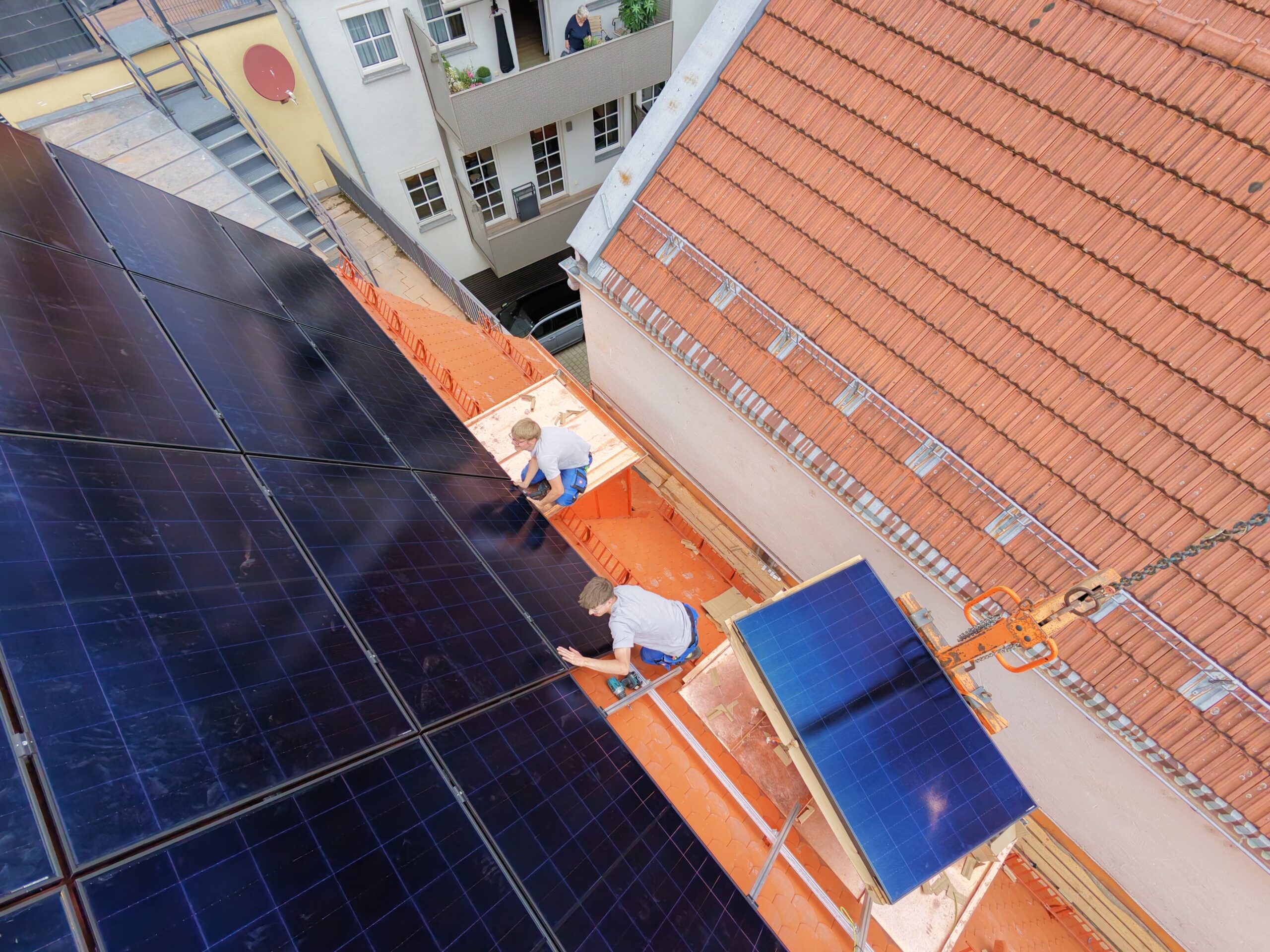 Zwei Monteure montieren Solarmodule auf Dach, Kran hebt Modul mit Vakuumheber