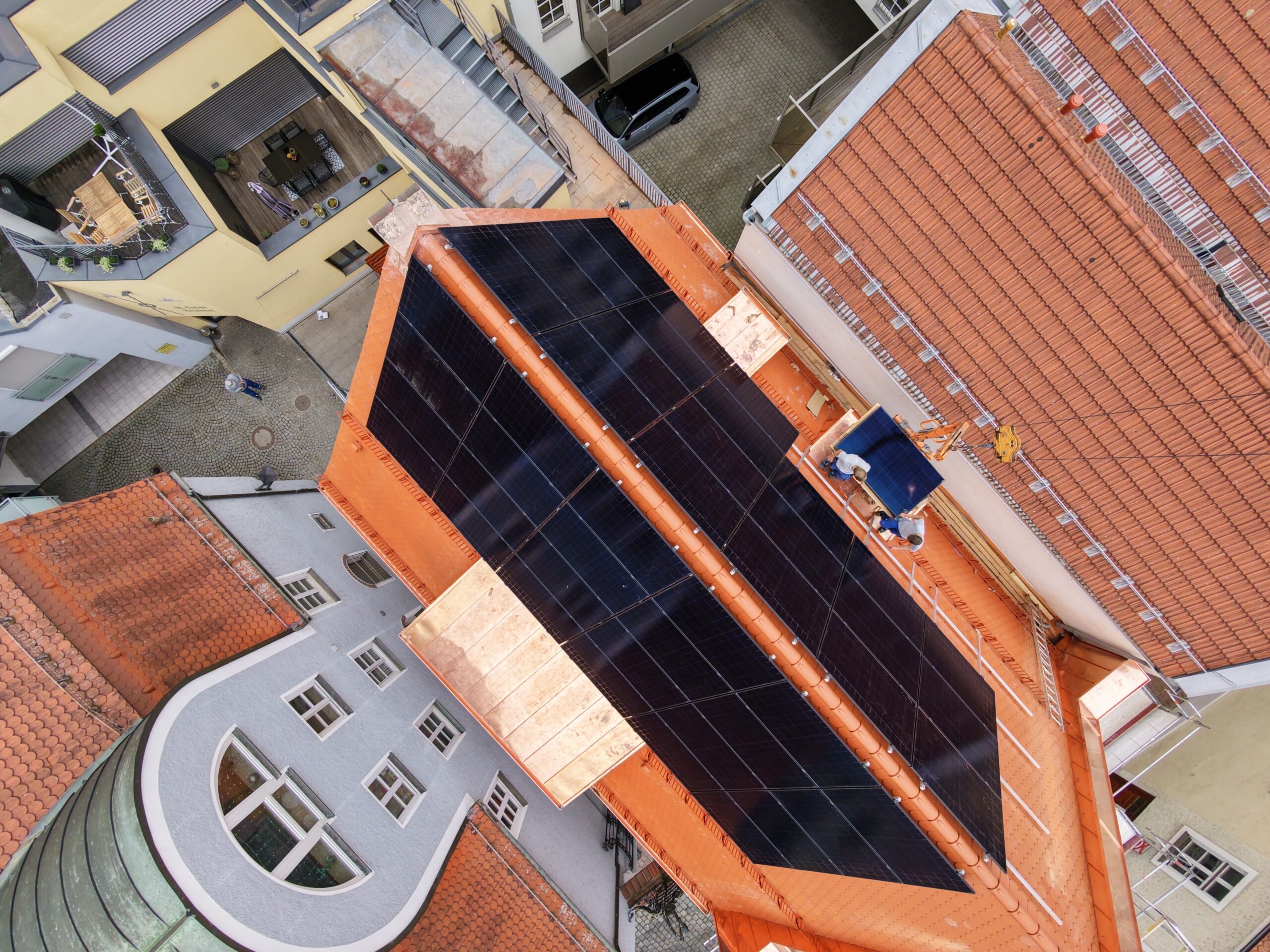 Vogelperspektive schwarzer Solarmodule auf orangem Ziegeldach im Altstadthof
